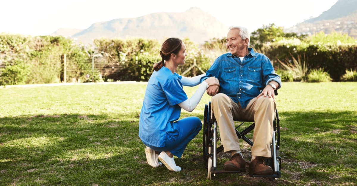 Caregiver supporting elderly person in wheelchair outdoors